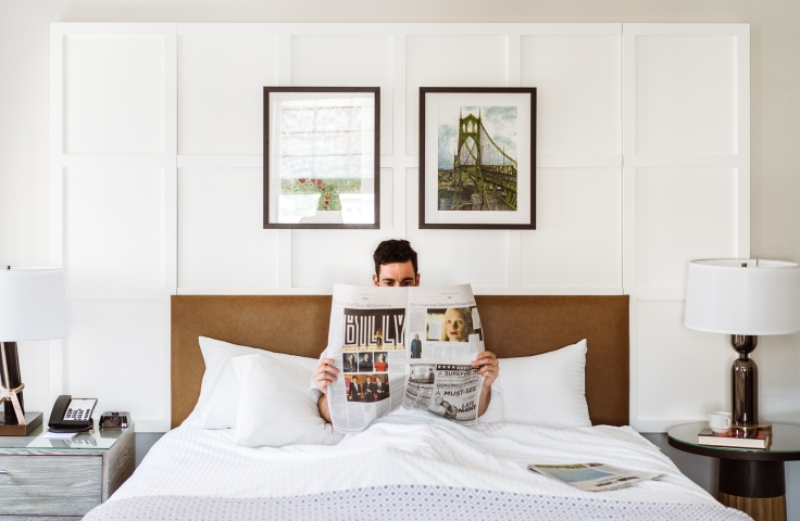 A man reading the paper in bed in his suite at the Heathman Hotel in Portland, Oregon.