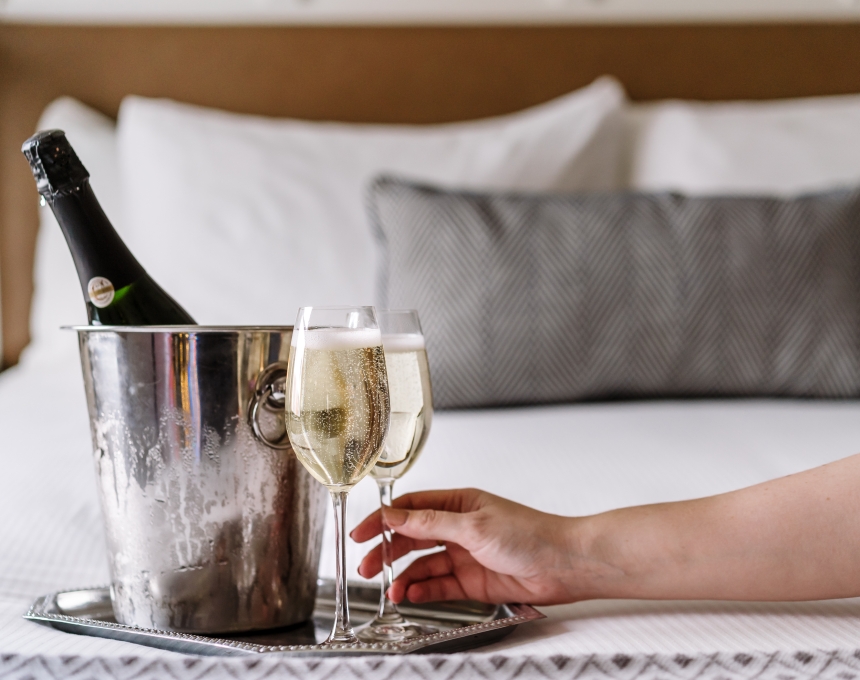 A silver tray with glasses and a bottle of champagne in an ice bucket on a hotel bed.