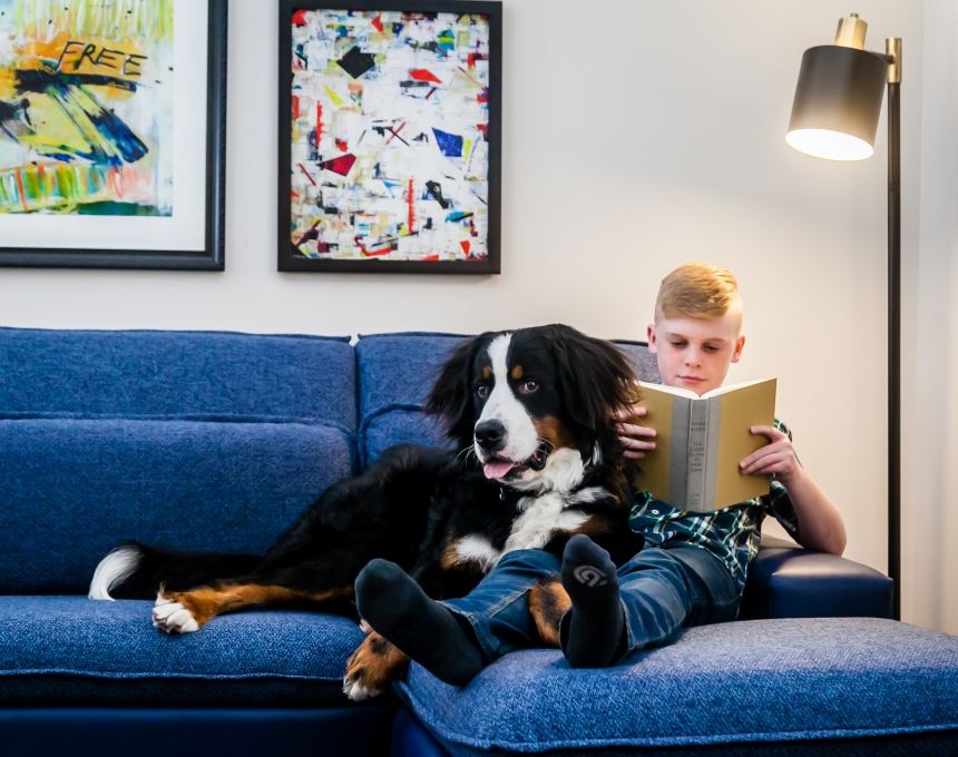 A young boy sitting with his dog on a couch and reading a book.