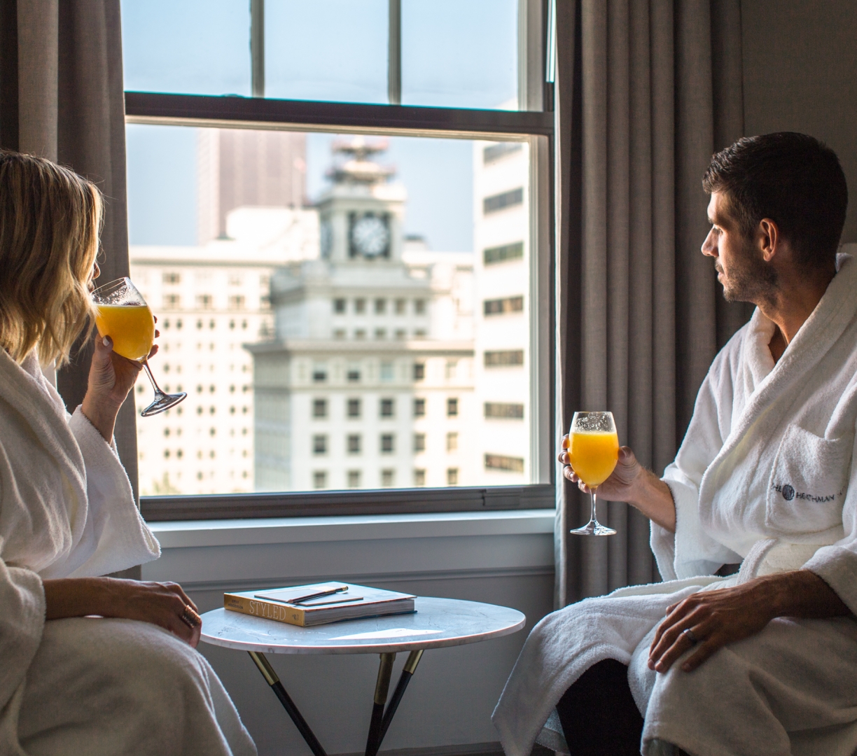 A couple in bath robes drinking mimosas and enjoying the view from their hotel suite.