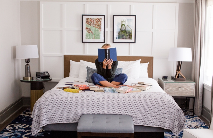 A woman reading on a bed surrounded by books.