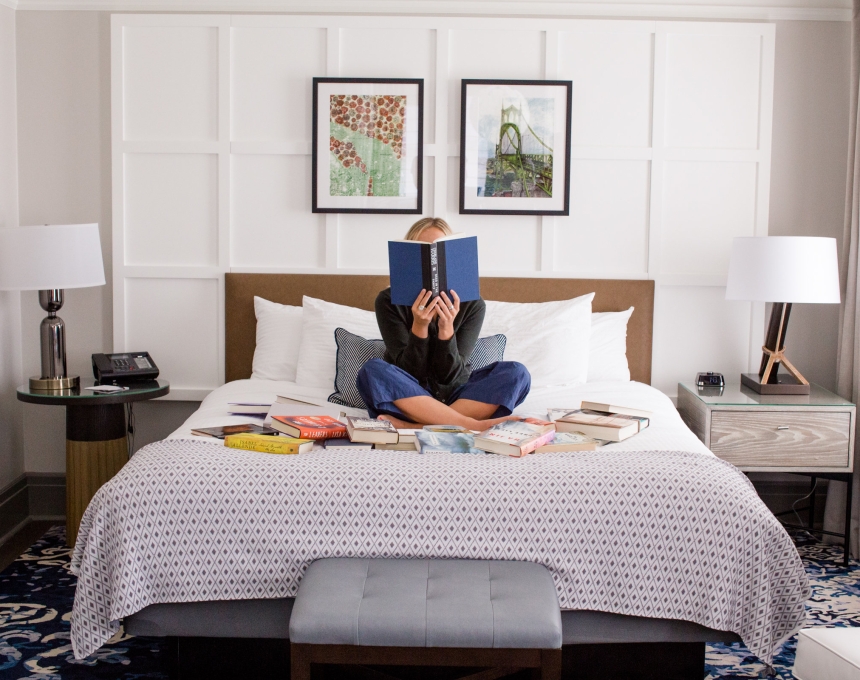 A woman reading on a bed surrounded by books.