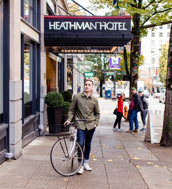 A young man with a bike standing under the Heathman Hotel awning.