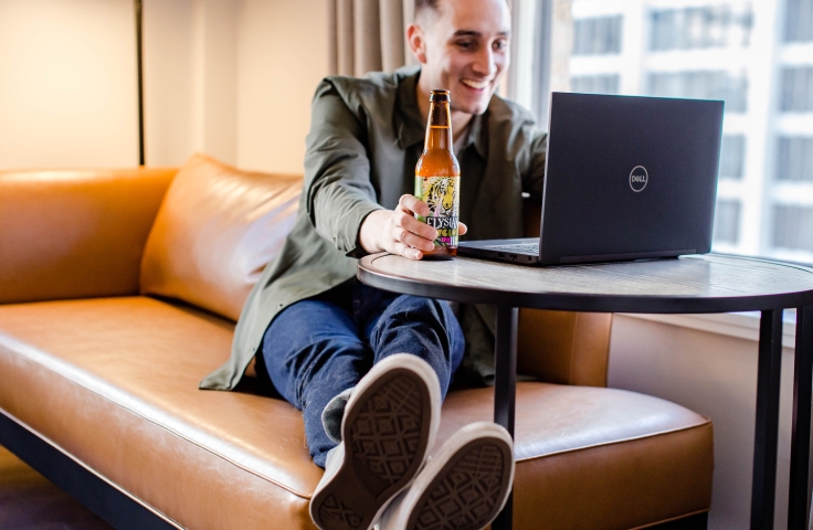 A man on a sofa drinking a beer while on his laptop.
