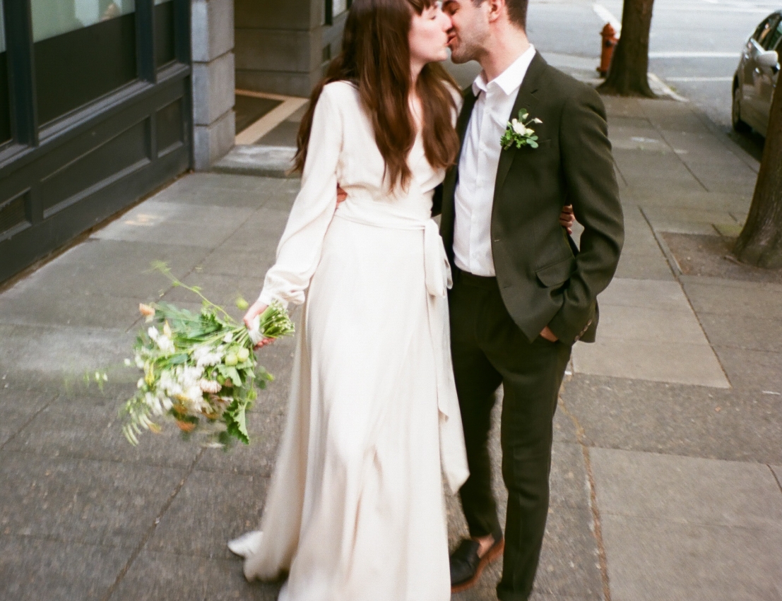 A bride and groom kissing on the sidewalk in front of the Heathman Hotel in Portland, Oregon.
