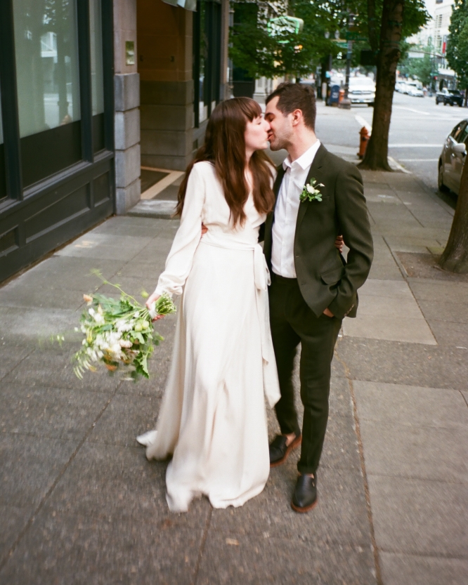 A bride and groom kissing on the sidewalk in front of the Heathman Hotel in Portland, Oregon.
