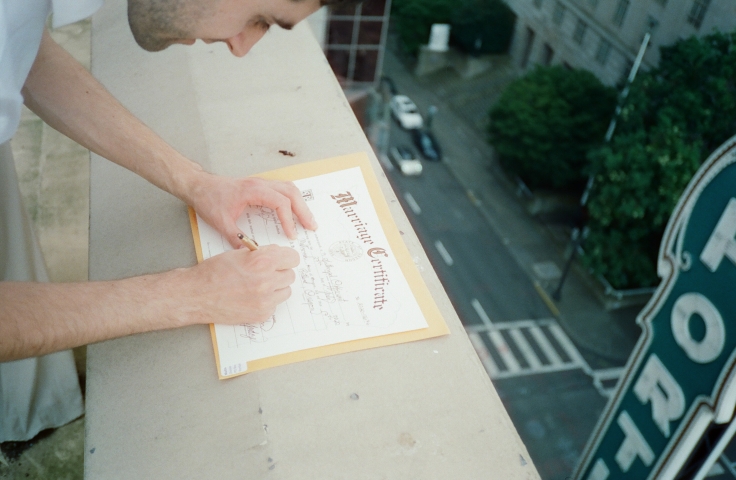 A man signing a wedding certificate on the ledge of a rooftop.