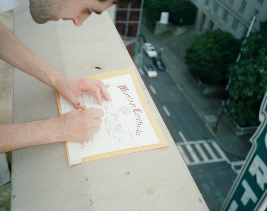 A man signing a wedding certificate on the ledge of a rooftop.