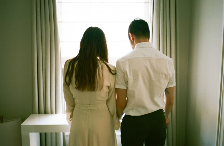A bride and groom looking out a window with their backs to the camera.